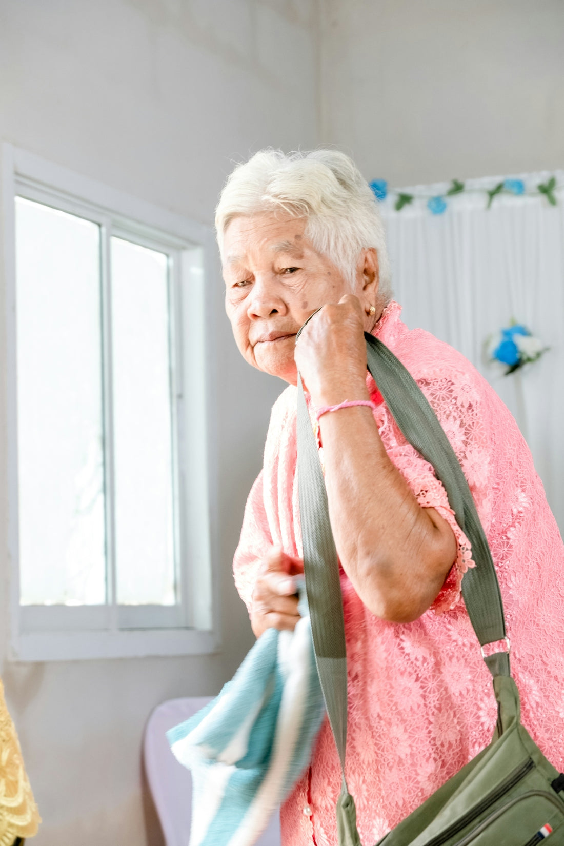 An elderly woman holds her bag, ready to leave.