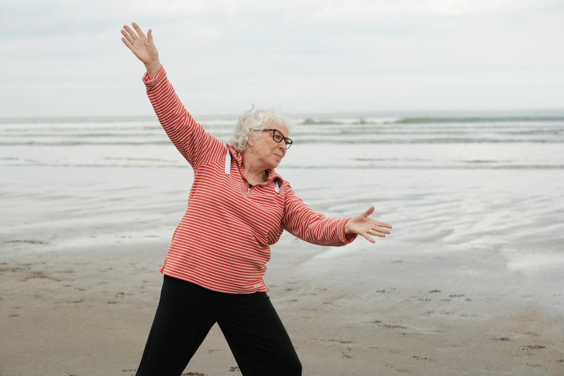 Woman exercises at the beach with outstretched arms.