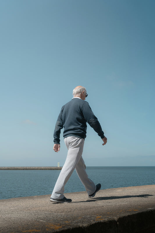 An elderly man walks by the sea.