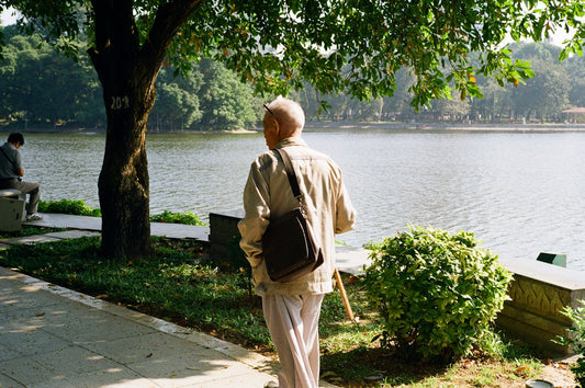 Elderly man walking by a lake in a park.